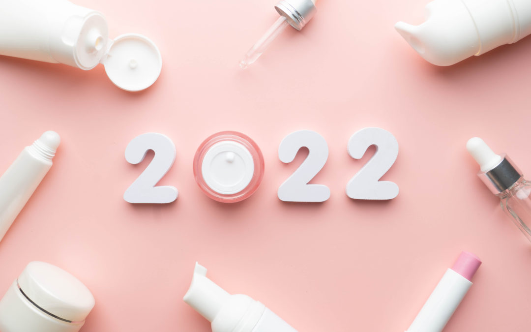 Flat lay of skincare products surrounding the year "2022" in white numbers on a soft pink background, symbolizing beauty trends or resolutions.