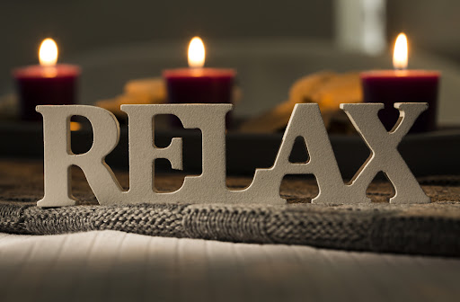 The word "relax" on a blanket in front of candles, for a blog from Advanced Skin + Body Lincoln Aesthetics and Spa