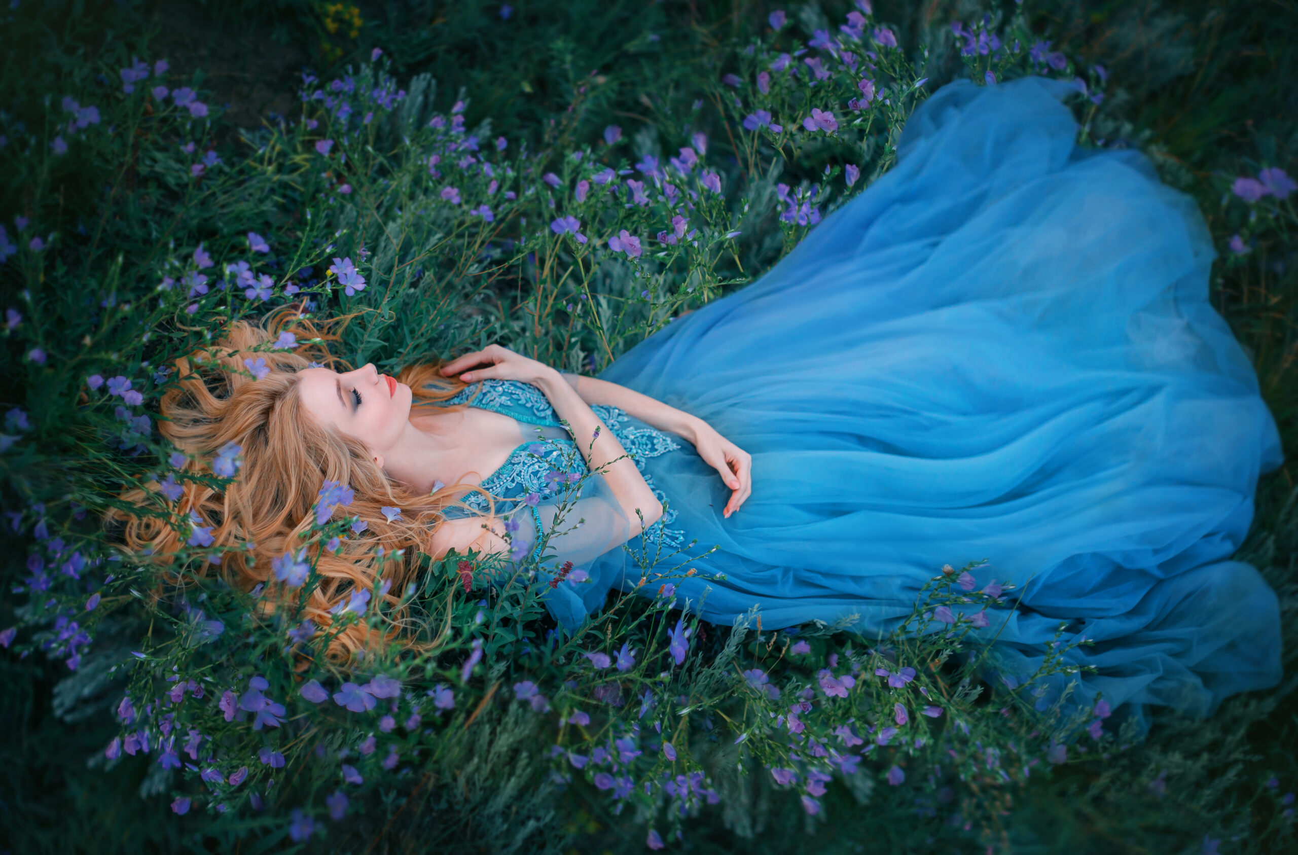Sleeping fairytale beauty in gown on bed of grass and flowers.